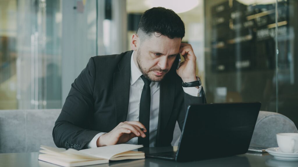 pexels photo 36766672 36766672 Focused businessman in suit multitasking on phone and laptop in modern office.