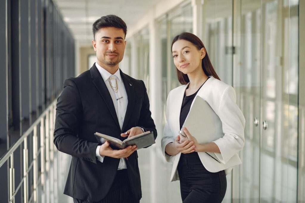 Mastering the First Impression: Your intriguing post title goes here Confident well dressed multiracial coworkers standing in modern office corridor while holding laptop and notebook in hands and looking at camera
