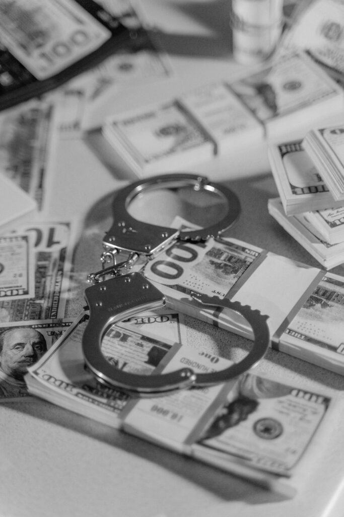 pexels photo 6266771 6266771 Black and white image of handcuffs placed over stacks of US dollar bills, symbolizing financial crime.