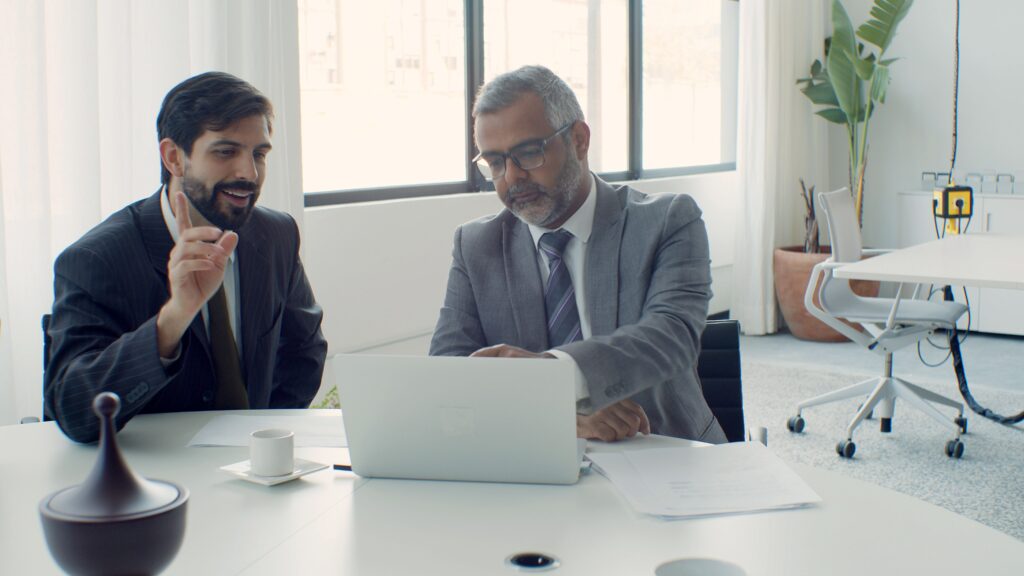 pexels photo 8463148 8463148 Two businessmen discussing projects on a laptop in a modern, bright office setting.